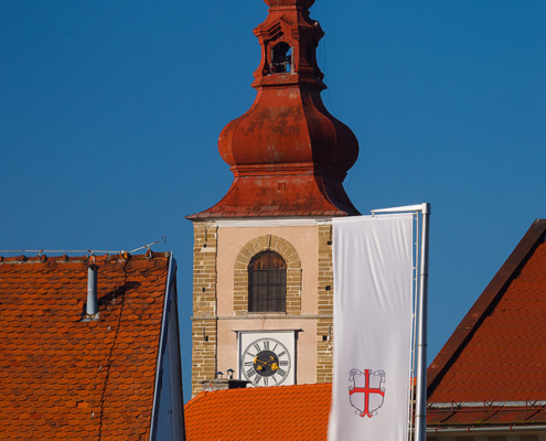 The tower of Church of Saint George and the flag with coat of arms of Ptuj in an afternoon light.