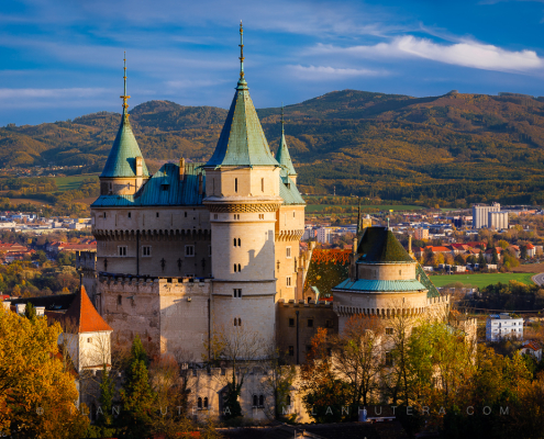 Wide autumn panorama of Bojnice Castle with colorful trees and mountains in the background