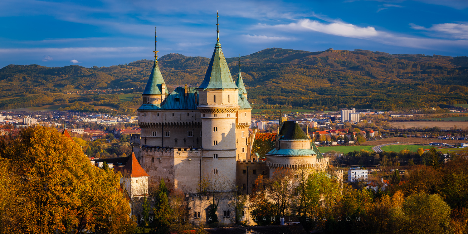 Wide autumn panorama of Bojnice Castle with colorful trees and mountains in the background