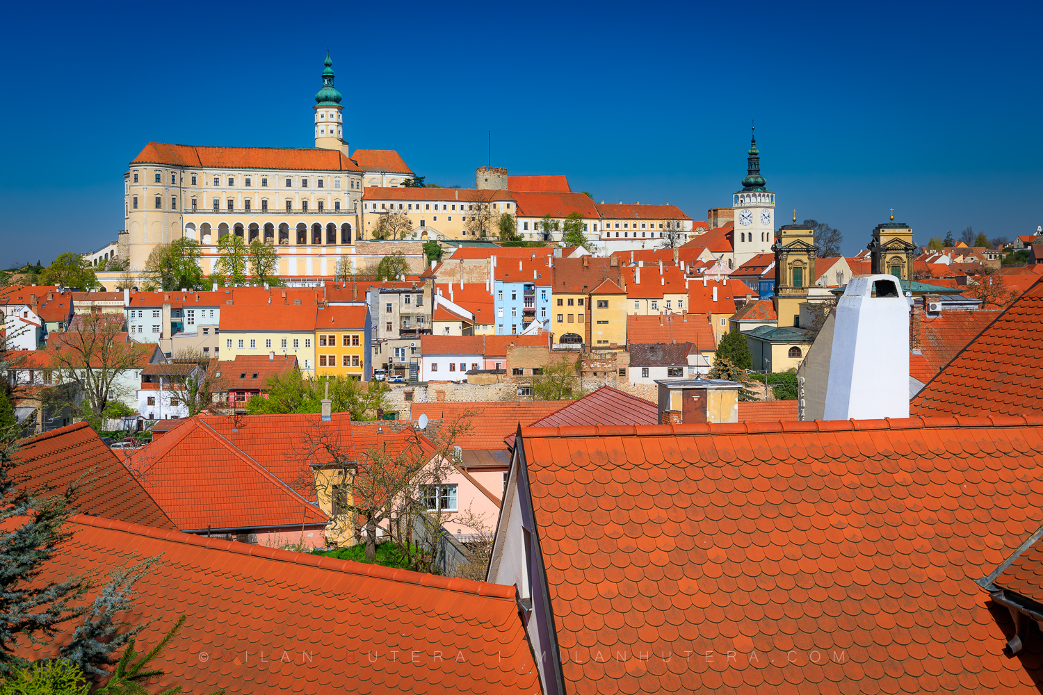 View of red rooftops in Mikulov, Czech Republic, with Mikulov Castle under a clear blue sky, shot from the steps to Svatý kopeček
