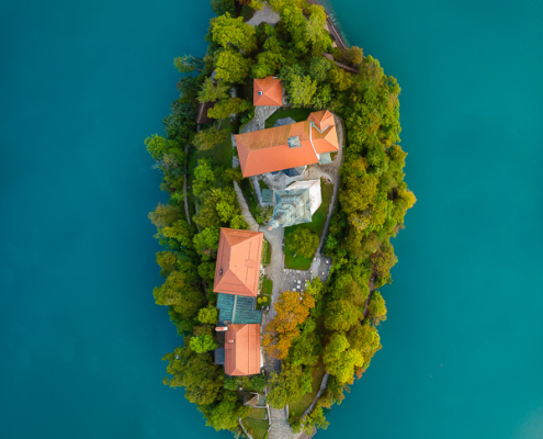 A vertical top-down aerial drone photograph of Bled Island surrounded by emerald waters of Bled Lake in Slovenia