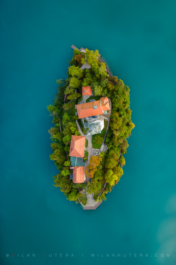 A vertical top-down aerial drone photograph of Bled Island surrounded by emerald waters of Bled Lake in Slovenia
