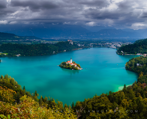 Panoramic view of Bled Lake from Mala Osojnica viewpoint with turquoise water, the island church, and storm clouds