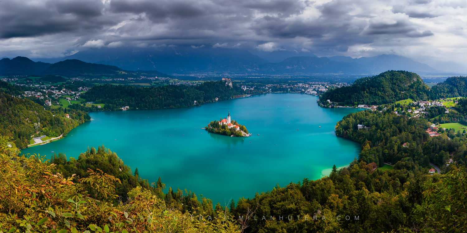 Panoramic view of Bled Lake from Mala Osojnica viewpoint with turquoise water, the island church, and storm clouds
