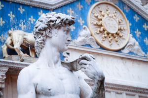 Close-up photograph of the David statue replica in front of the ornate blue and gold facade of Palazzo Vecchio in Florence, Italy