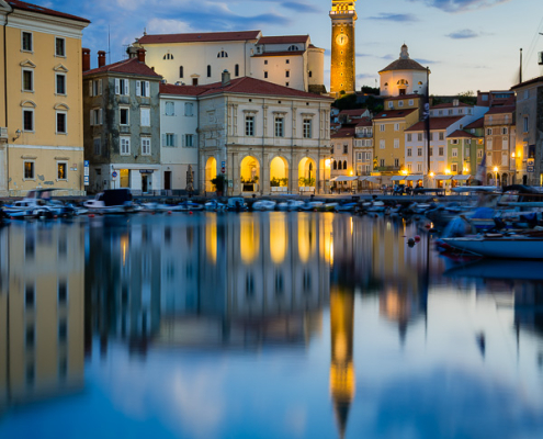 Dawn reflection of St. George's Parish Church bell tower and historic town buildings in Piran harbor, Slovenia.