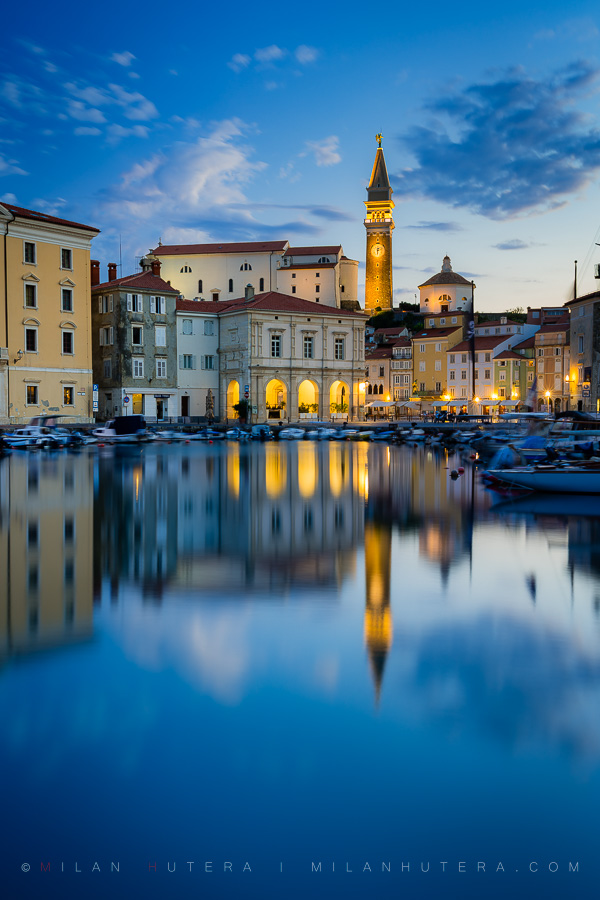 Dawn reflection of St. George's Parish Church bell tower and historic town buildings in Piran harbor, Slovenia.
