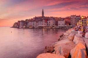 Rovinj, Croatia in pink sunset light with people watching the sun go down from the rocky pier