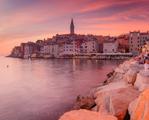 Rovinj, Croatia in pink sunset light with people watching the sun go down from the rocky pier