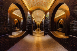 Symmetrical wide-angle interior of the 1874 Žlutý kopec water reservoir in Brno, showcasing illuminated red brick arches, dark pillars, and curved floors.