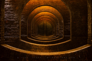 A geometric perspective looking centrally through a row of brick arches and inverted barrel vaults inside the 1874 Žlutý kopec water reservoir.