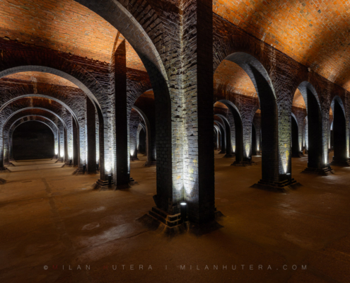 An asymmetrical, wide-angle interior photograph of the 1894 Žlutý Kopec water reservoir in Brno, showcasing a vast forest of brick pillars and cross-vaulted ceilings.