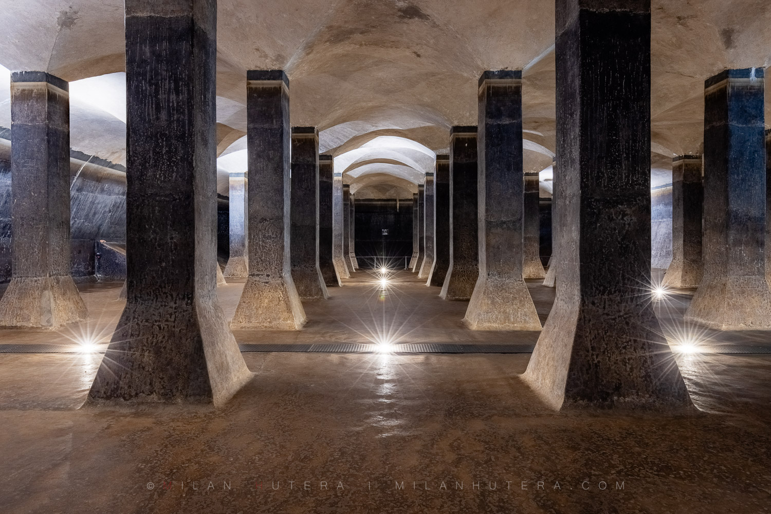 1917 Žlutý Kopec Water Reservoir, Brno, Czech Republic Symmetrical interior view of the monolythic 1917 Žlutý kopec water reservoir in Brno, showing massive concrete pillars and groin vaulted ceilings with starburst lighting.