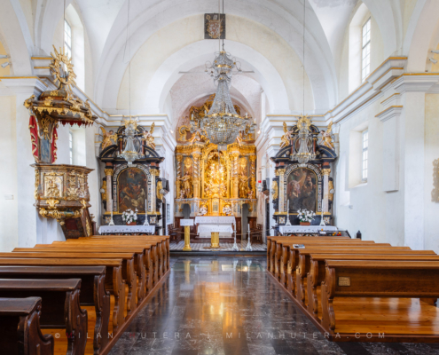 Bled Island church interior featuring wooden pews, a large crystal chandelier, and a magnificent golden Baroque altar