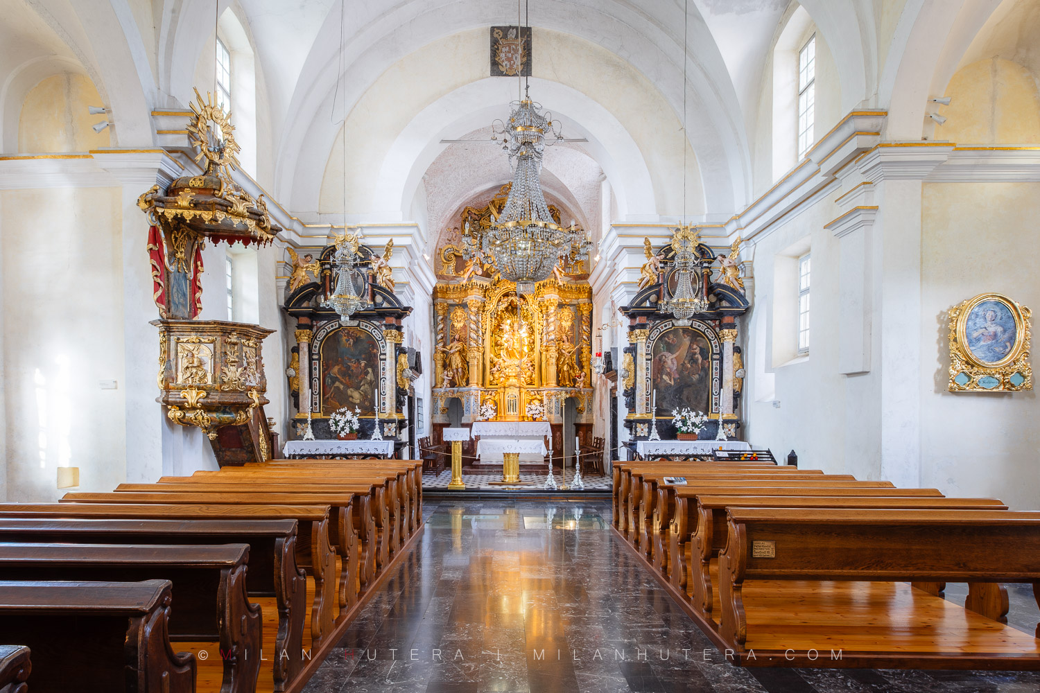 Bled Island church interior featuring wooden pews, a large crystal chandelier, and a magnificent golden Baroque altar