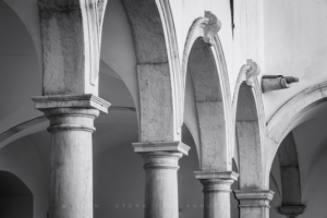 Black and white architectural photography of the Minorite monastery arches in Piran, Slovenia, showcasing the historic Renaissance cloister columns.