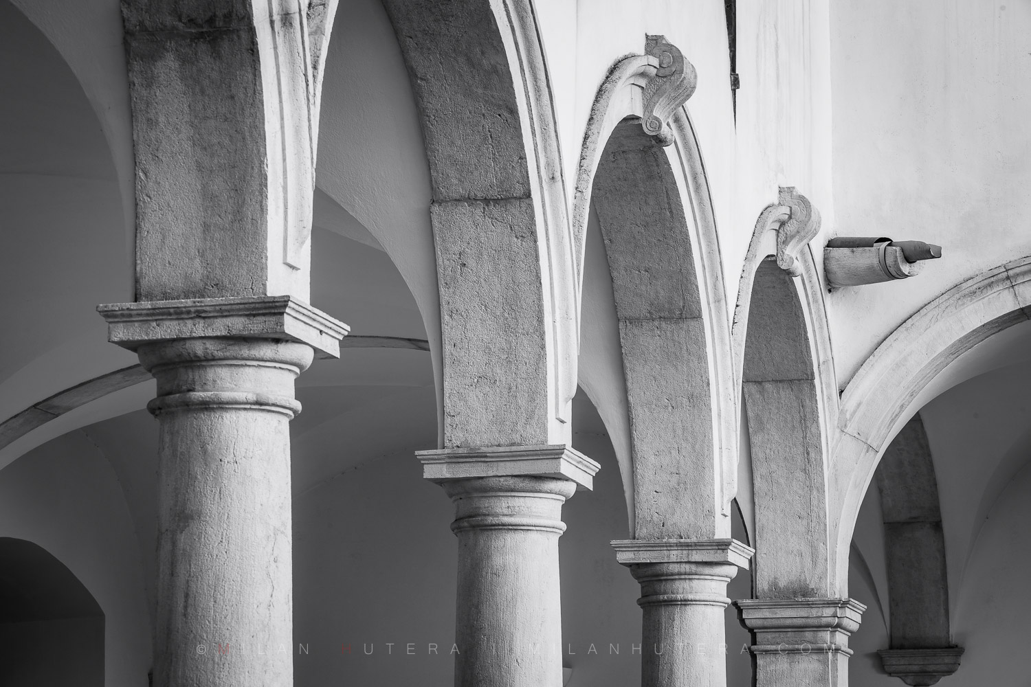 Black and white architectural photography of the Minorite monastery arches in Piran, Slovenia, showcasing the historic Renaissance cloister columns.
