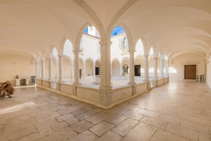 Wide-angle photography of the Minorite monastery courtyard in Piran, Slovenia, showing the beautiful Renaissance cloister, stone well, and vaulted arcades.