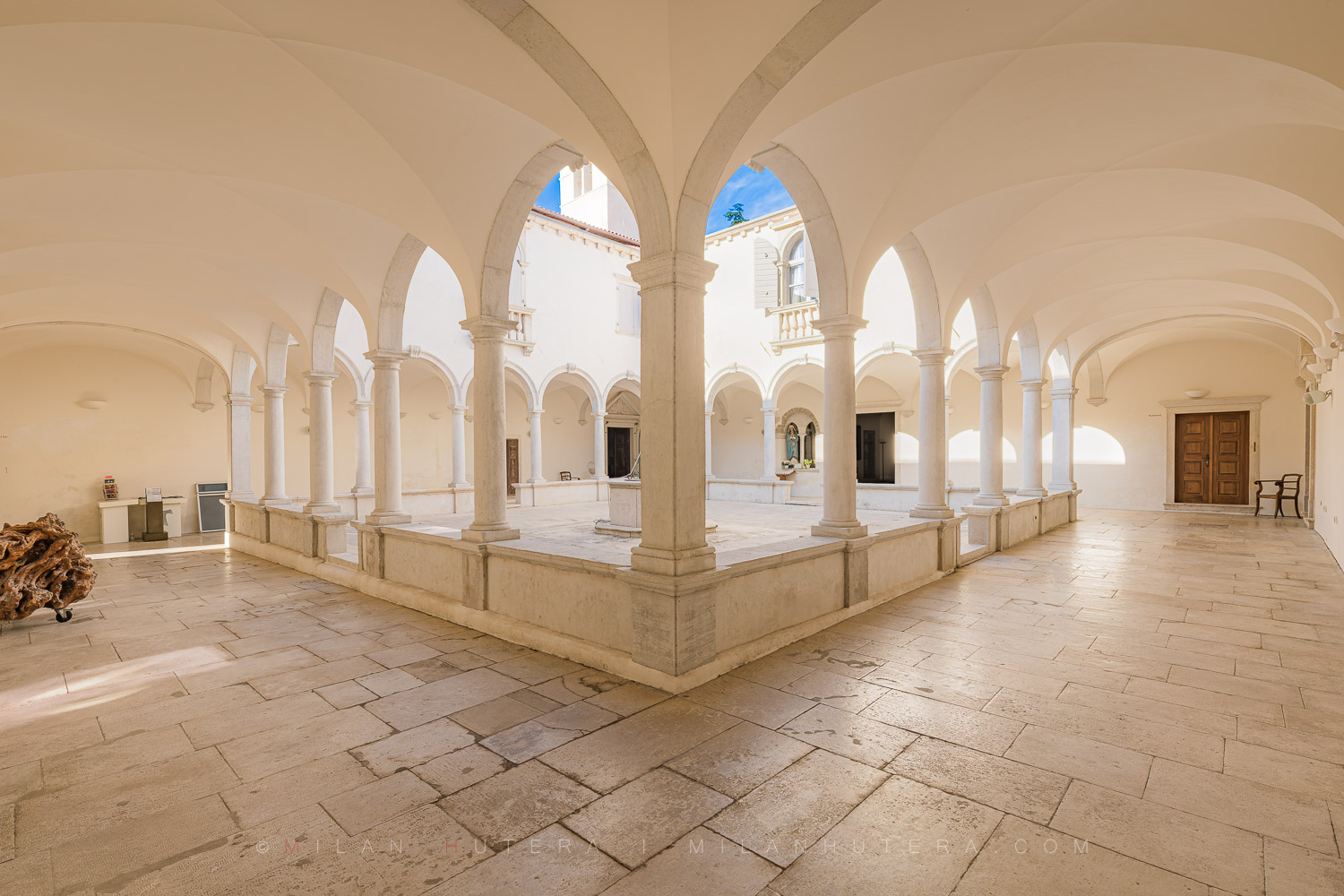 Wide-angle photography of the Minorite monastery courtyard in Piran, Slovenia, showing the beautiful Renaissance cloister, stone well, and vaulted arcades.
