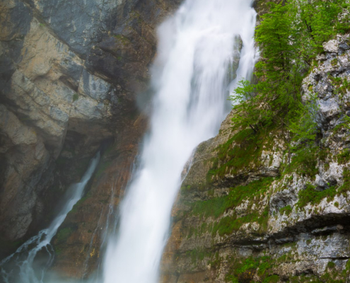 Savica waterfall rushing down a steep cliff into a vibrant emerald pool