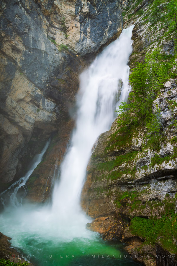 Savica waterfall rushing down a steep cliff into a vibrant emerald pool