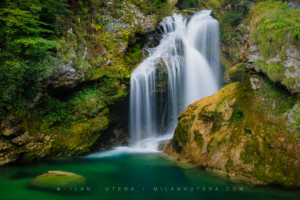 Šum Waterfall cascading into a deep emerald green pool surrounded by mossy rocks in Vintgar Gorge, Slovenia
