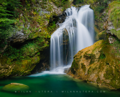Šum Waterfall cascading into a deep emerald green pool surrounded by mossy rocks in Vintgar Gorge, Slovenia