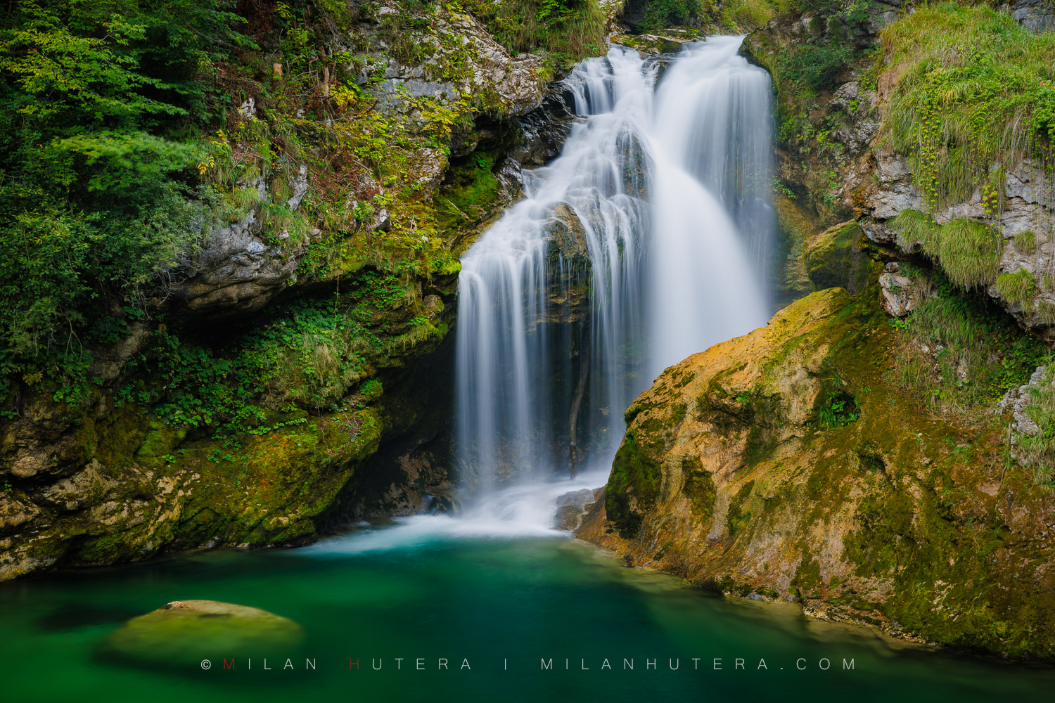Šum Waterfall cascading into a deep emerald green pool surrounded by mossy rocks in Vintgar Gorge, Slovenia