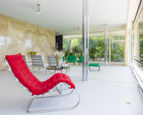 Villa Tugendhat living room featuring red chaise longue, Barcelona chairs, and translucent onyx wall
