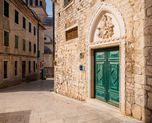Empty Šibenik old town street with a Gothic portal and the dome of St. James Cathedral in the background